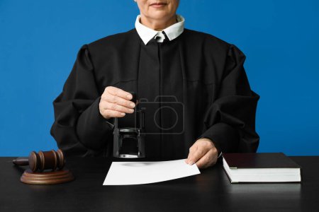 Photo for Female judge with stamp and document at table on blue background - Royalty Free Image