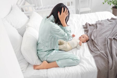 Junge Frau mit Baby leidet an postnataler Depression im Schlafzimmer