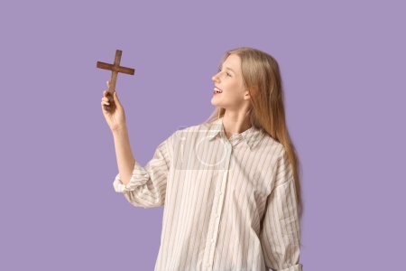 Foto de Hermosa joven feliz mujer con cruz de madera sobre fondo púrpura - Imagen libre de derechos