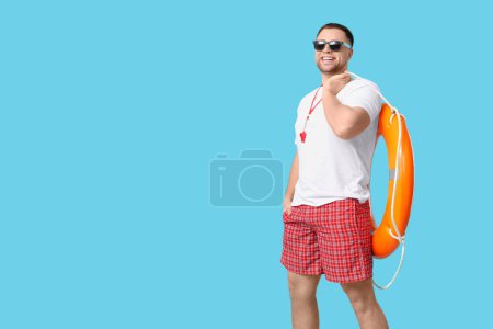 Photo for Happy young lifeguard in sunglasses with lifebuoy on blue background - Royalty Free Image