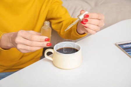 Foto de Mujer madura dejando caer el aceite de CBD en la taza de café en casa, primer plano - Imagen libre de derechos