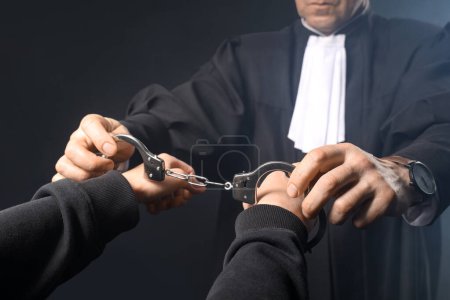 Photo for Mature judge putting handcuffs on suspect against dark background, closeup - Royalty Free Image