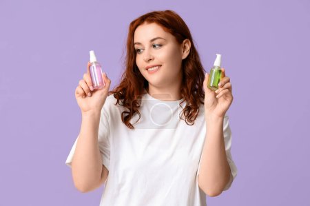 Schöne junge glückliche Frau mit Flaschen Desinfektionsmittel auf lila Hintergrund