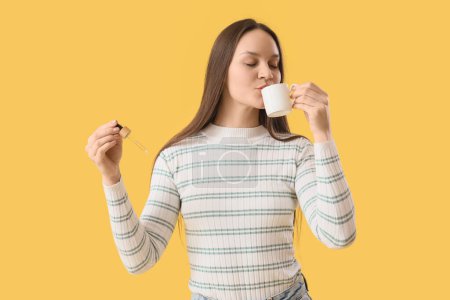 Foto de Mujer joven con aceite de CBD tomando café sobre fondo amarillo - Imagen libre de derechos