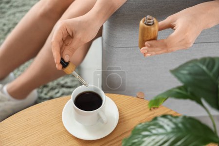 Foto de Mujer joven dejando caer el aceite de CBD en la taza de café en casa, primer plano - Imagen libre de derechos