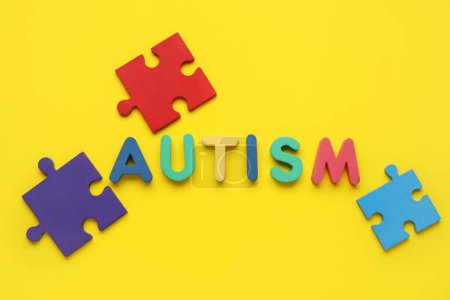Word AUTISM and colorful puzzle pieces on yellow background. Top view