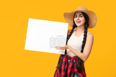 Schöne junge glückliche Frau, die auf ein leeres Plakat auf gelbem Hintergrund zeigt. Fest Junina (Juni-Fest)
