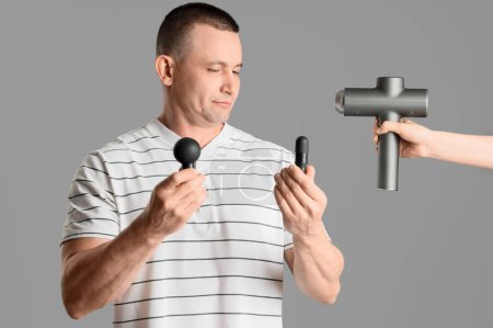 Young man with attachments and percussive massager on light background