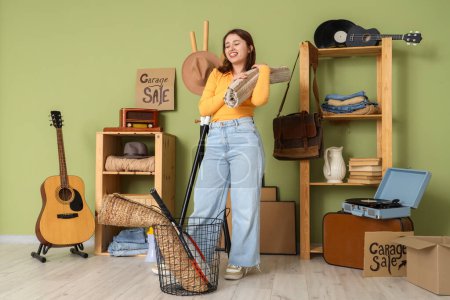 Photo for Young woman with rolled carpet for garage sale in room of unwanted stuff - Royalty Free Image