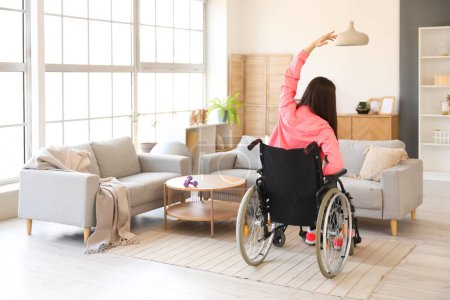 Sporty young woman in wheelchair training at home, back view