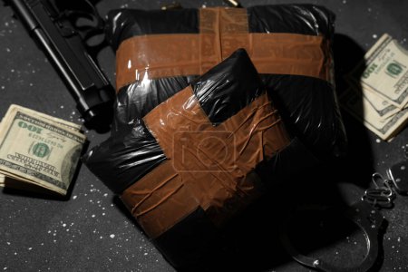 Drogenpakete mit Waffe und Geld auf dunklem Hintergrund, Nahaufnahme