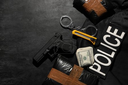 Drogenpakete mit Waffe, Geld und Polizeiuniform auf dunklem Hintergrund