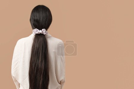 Woman with ponytail and silk scrunchy on beige background, back view