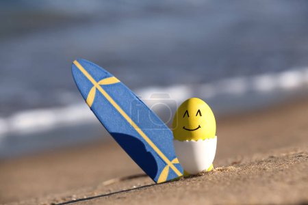 Painter Easter egg and surfboard on sea beach