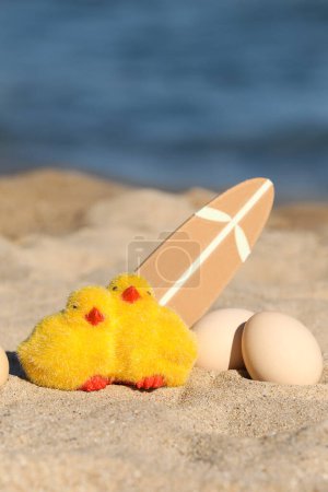Toy chicks, painter Easter eggs and surfboard on sea beach