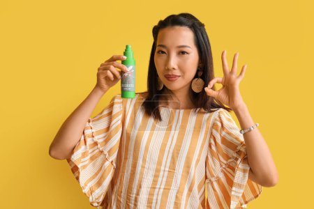 Young Asian woman with mosquito repellent showing OK on yellow background