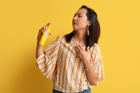 Young Asian woman with mosquito repellent on yellow background