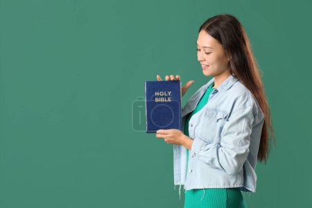 Foto de Hermosa mujer asiática joven con Biblia sobre fondo verde - Imagen libre de derechos