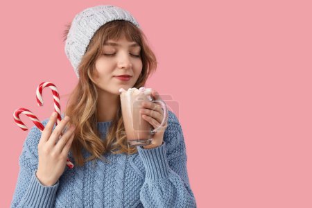 Foto de Mujer bastante joven con bastones de caramelo bebiendo taza de chocolate caliente sobre fondo rosa - Imagen libre de derechos