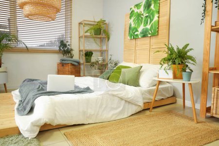 Téléchargez les photos : Intérieur de la chambre avec des plantes vertes et ordinateur portable sur le lit - en image libre de droit