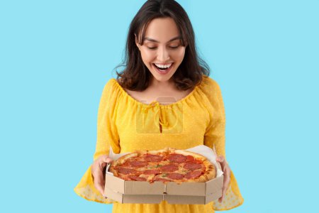 Junge Frau mit leckerer Pfefferoni-Pizza auf blauem Hintergrund