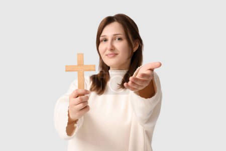 Religious young woman with wooden cross reaching out hand on white background