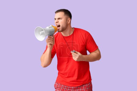 Photo for Young lifeguard with whistle shouting into megaphone on lilac background - Royalty Free Image
