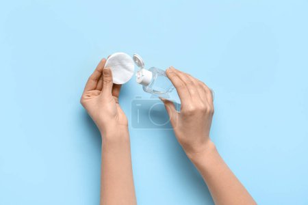 Female hands with bottle of sanitizer and cotton pad on blue background