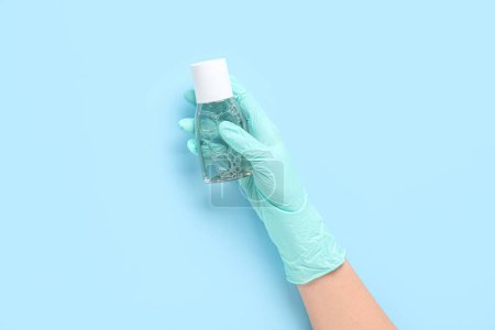 Female hand in gloves with bottle of sanitizer on blue background