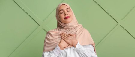 Young Muslim woman in hijab meditating on green background. Zen concept