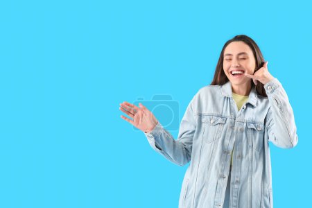 Cool young woman showing "call me" gesture on light blue background
