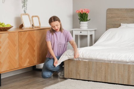 Pretty young woman making bed in modern bedroom
