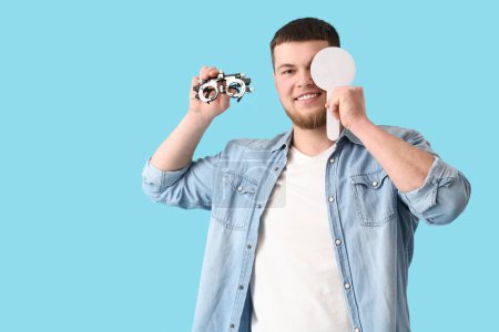 Young man with eye occluder and trial frame on blue background