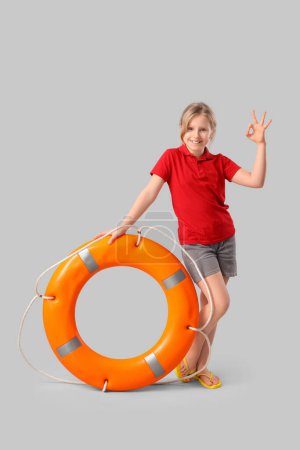 Photo for Happy little girl lifeguard with ring buoy showing OK gesture on grey background - Royalty Free Image