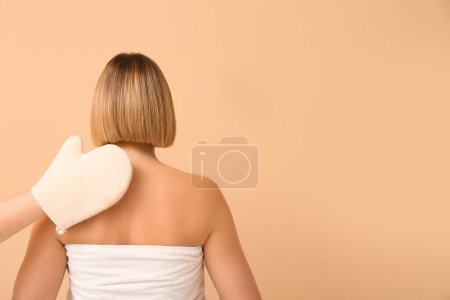 Schöne junge Frau und Hand mit Körpermassagehandschuh auf beigem Hintergrund, Rückseite