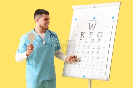 Foto de Oftalmólogo masculino con oclusor y tabla de pruebas oculares sobre fondo amarillo - Imagen libre de derechos