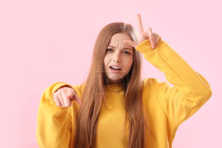 Junge Frau im Kapuzenpullover zeigt Verlierer-Geste und zeigt auf Betrachter auf rosa Hintergrund