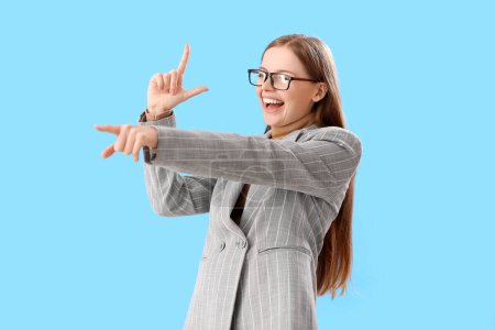 Photo for Young businesswoman showing loser gesture and pointing at something on blue background - Royalty Free Image