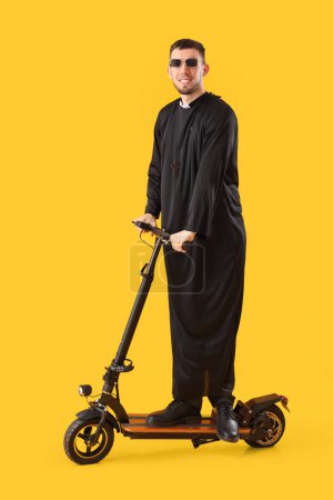 Sacerdote joven con scooter eléctrico sobre fondo amarillo