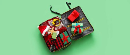 Koffer mit warmer Kleidung und Weihnachtsgeschenken auf grünem Hintergrund. Winterferienkonzept