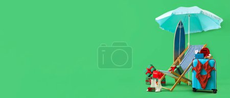 Koffer, Sonnenschirm, Liegestuhl, Surfbrett und Weihnachtsgeschenke auf grünem Hintergrund mit Platz für Text. Winterferienkonzept
