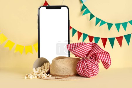 Téléphone portable avec écran blanc, chapeau, paquet et pop-corn sur fond beige