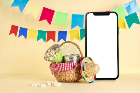 Mobile phone with blank screen, basket, popcorn and sombrero on beige background