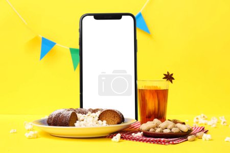 Foto de Teléfono móvil con pantalla en blanco y comida tradicional sobre fondo amarillo - Imagen libre de derechos