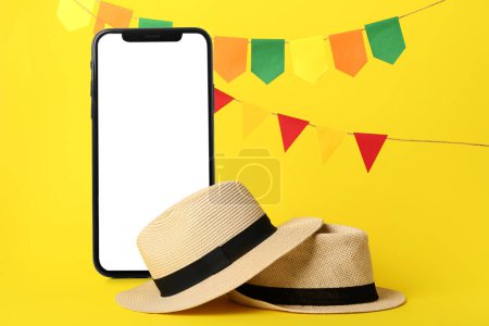 Mobile phone with blank screen and hats on yellow background