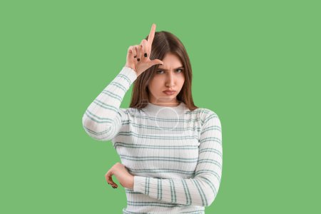 Photo for Sad young woman showing loser gesture on green background - Royalty Free Image