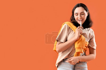 Foto de Mujer joven fumando cigarro electrónico sobre fondo naranja - Imagen libre de derechos