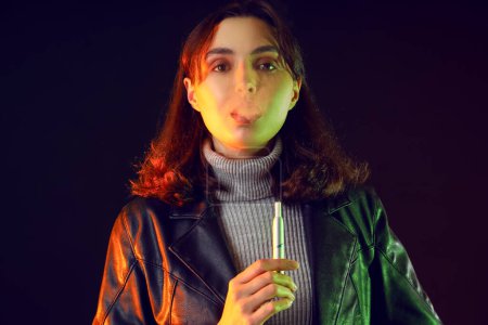 Téléchargez les photos : Jeune femme fumant cigare électronique sur fond sombre, gros plan - en image libre de droit