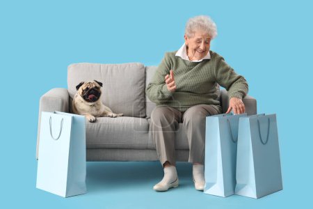 Senior woman with shopping bags and pug dog sitting on sofa against blue background