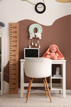 Stylish children's room interior with comfortable workspace, laptop and wooden stadiometer